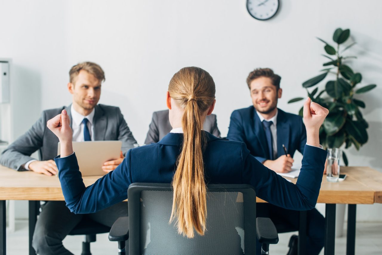 Selective focus of employee showing yeah gesture near smiling recruiters at table